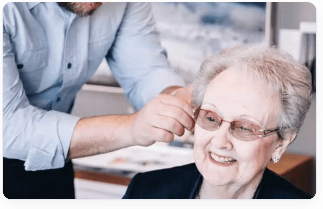 Audioprothésiste des Centres Masliah ajustant l'appareil auditif d'une dame âgée souriante